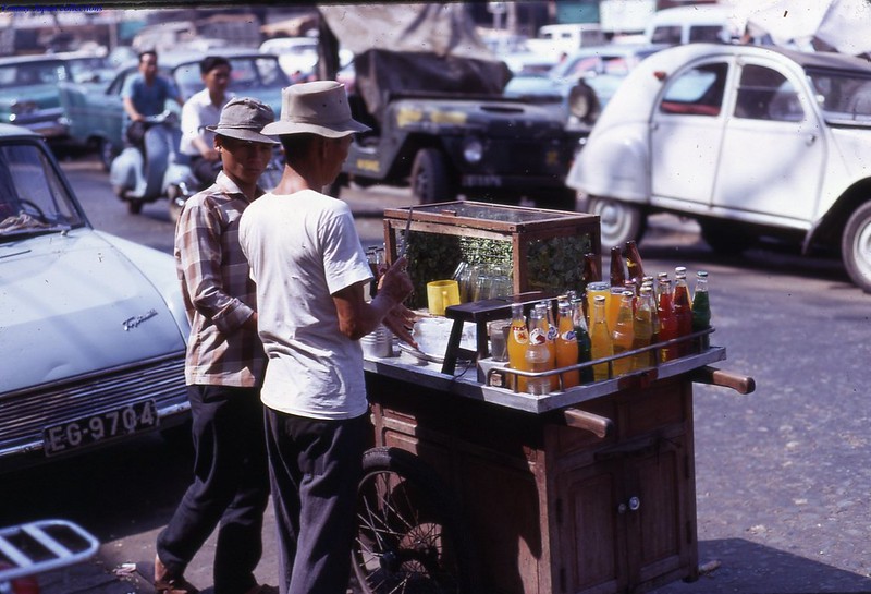 Sài Gòn 1969 - Hình ảnh một xe bán nước rau má, nước giải khát dạo trên đường phố Sài Gòn.Chai màu xanh bạc hà của hãng BGI - Người bán đang chặt đá, kế bên là thanh gỗ để làm đá bào (dành cho món xi rô đá bào mà học sinh rất yêu thích).